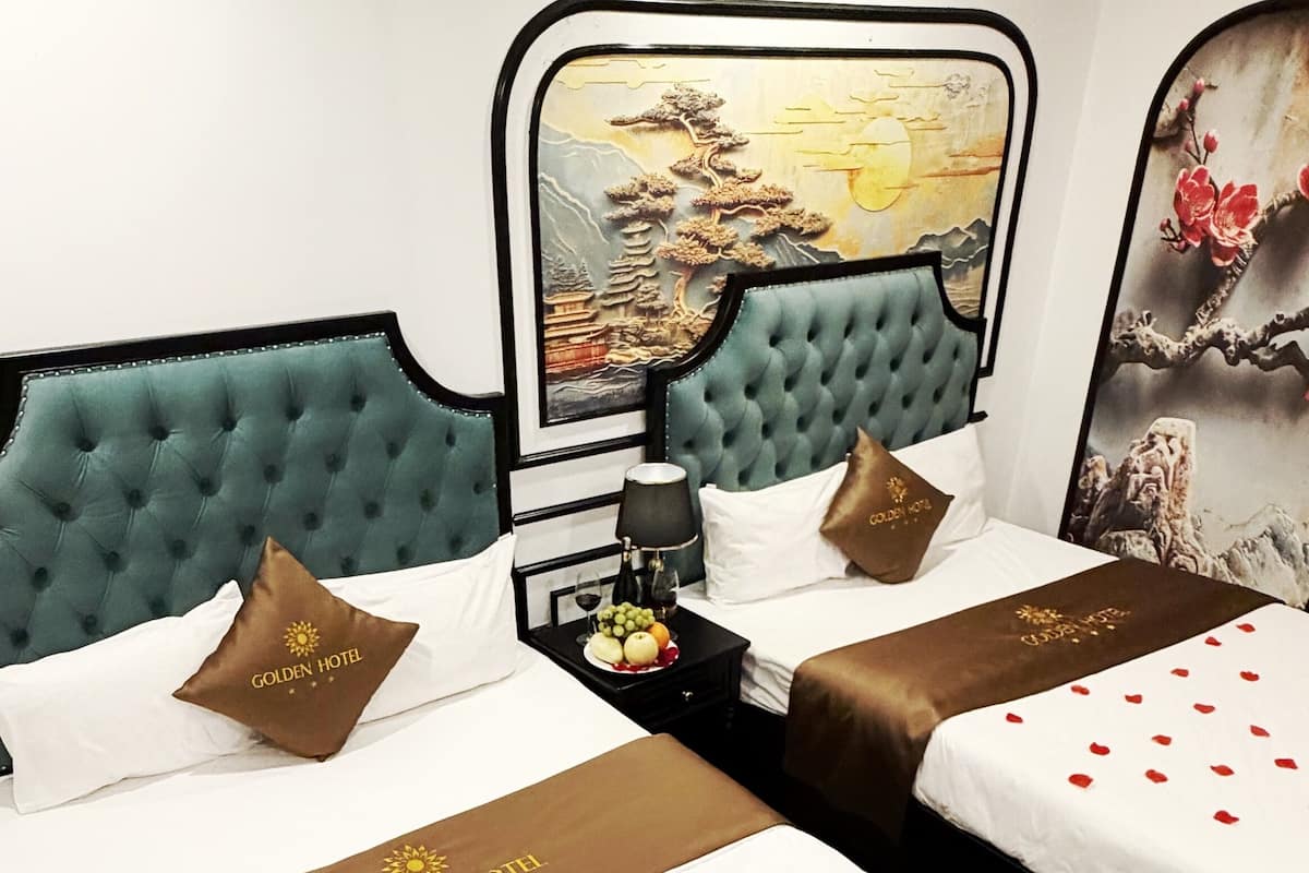 A hotel room with two beds, a nightstand with a lamp, a fruit plate, and a wall painting.