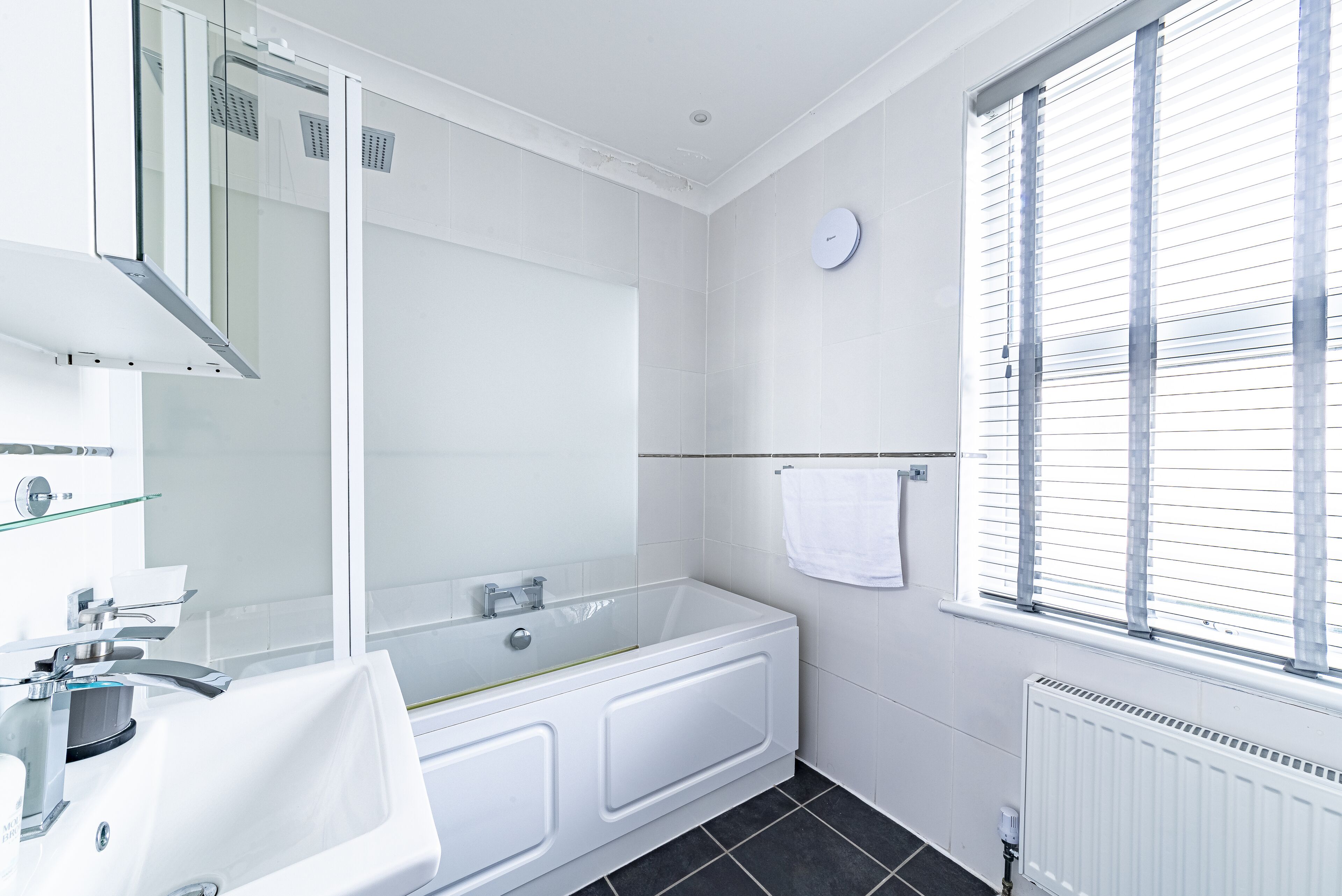 Un baño moderno con cabina de ducha de vidrio, una bañera blanca y un ventanal con persianas.