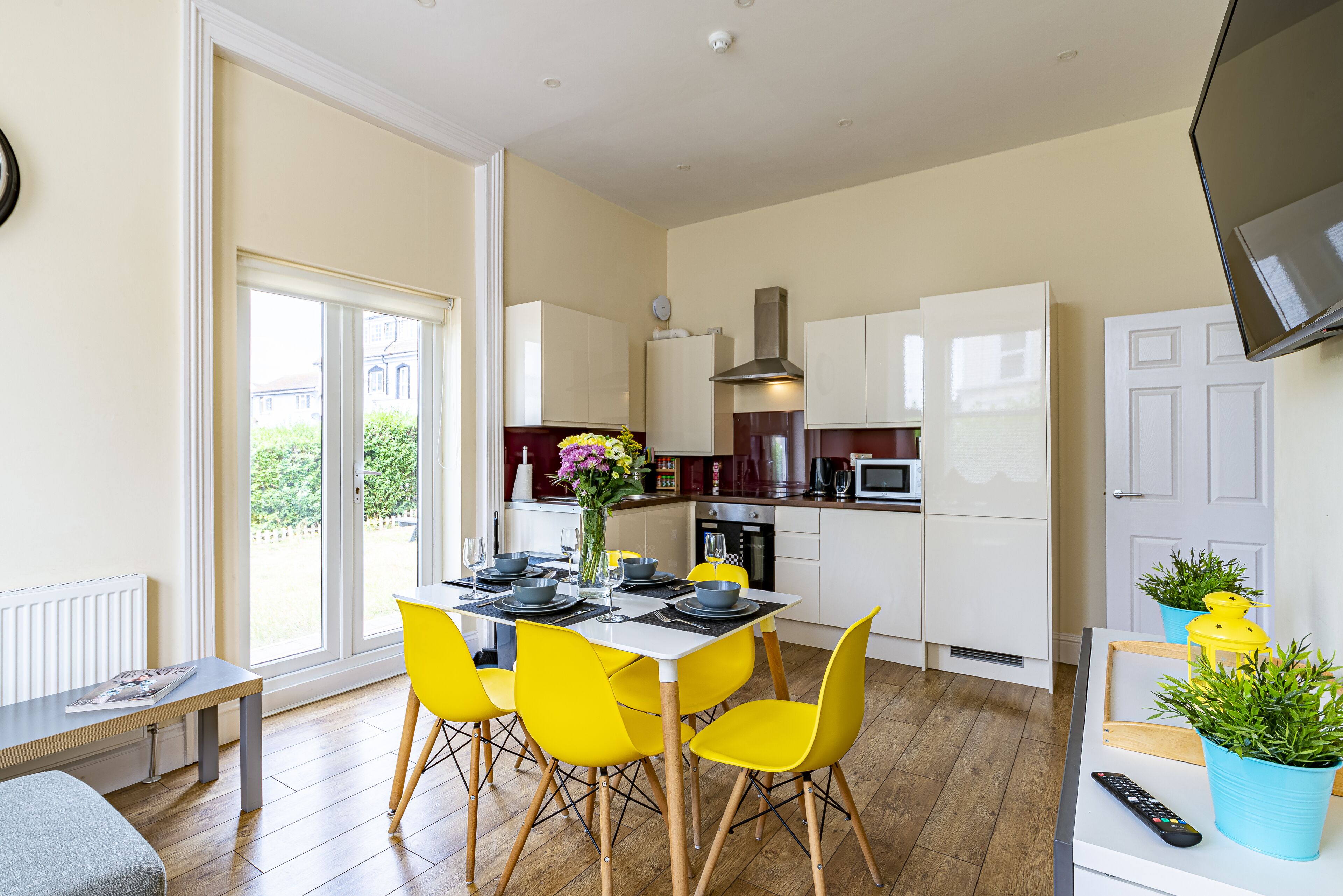 A modern kitchen with white cabinets, a dining table with yellow chairs, and a large window with a view of greenery.