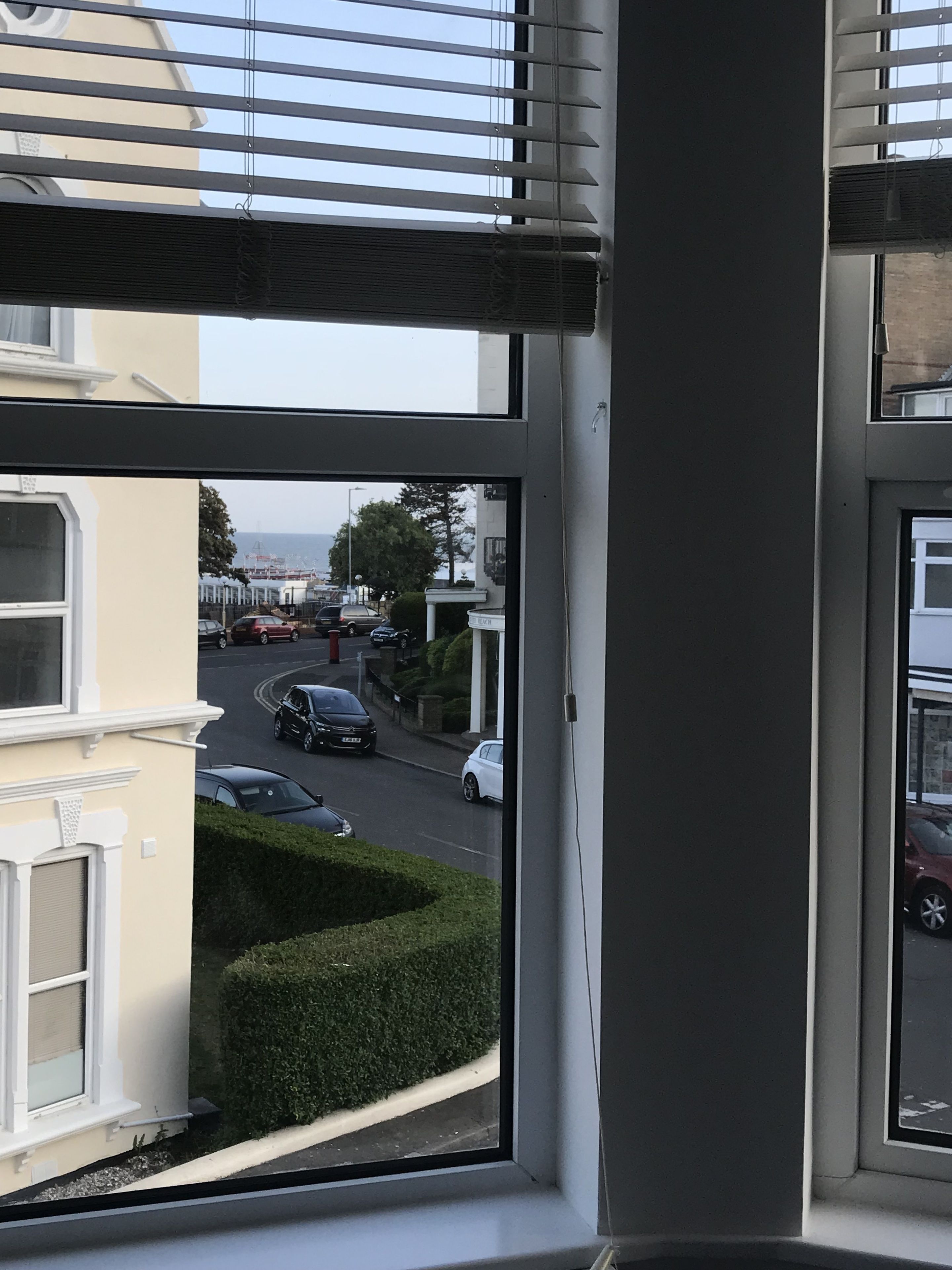 A view from a window overlooking a street with parked cars and a building in the background.