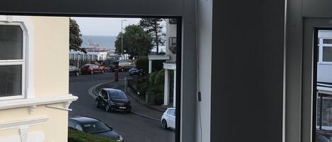 A view from a window overlooking a street with parked cars and a building in the background.