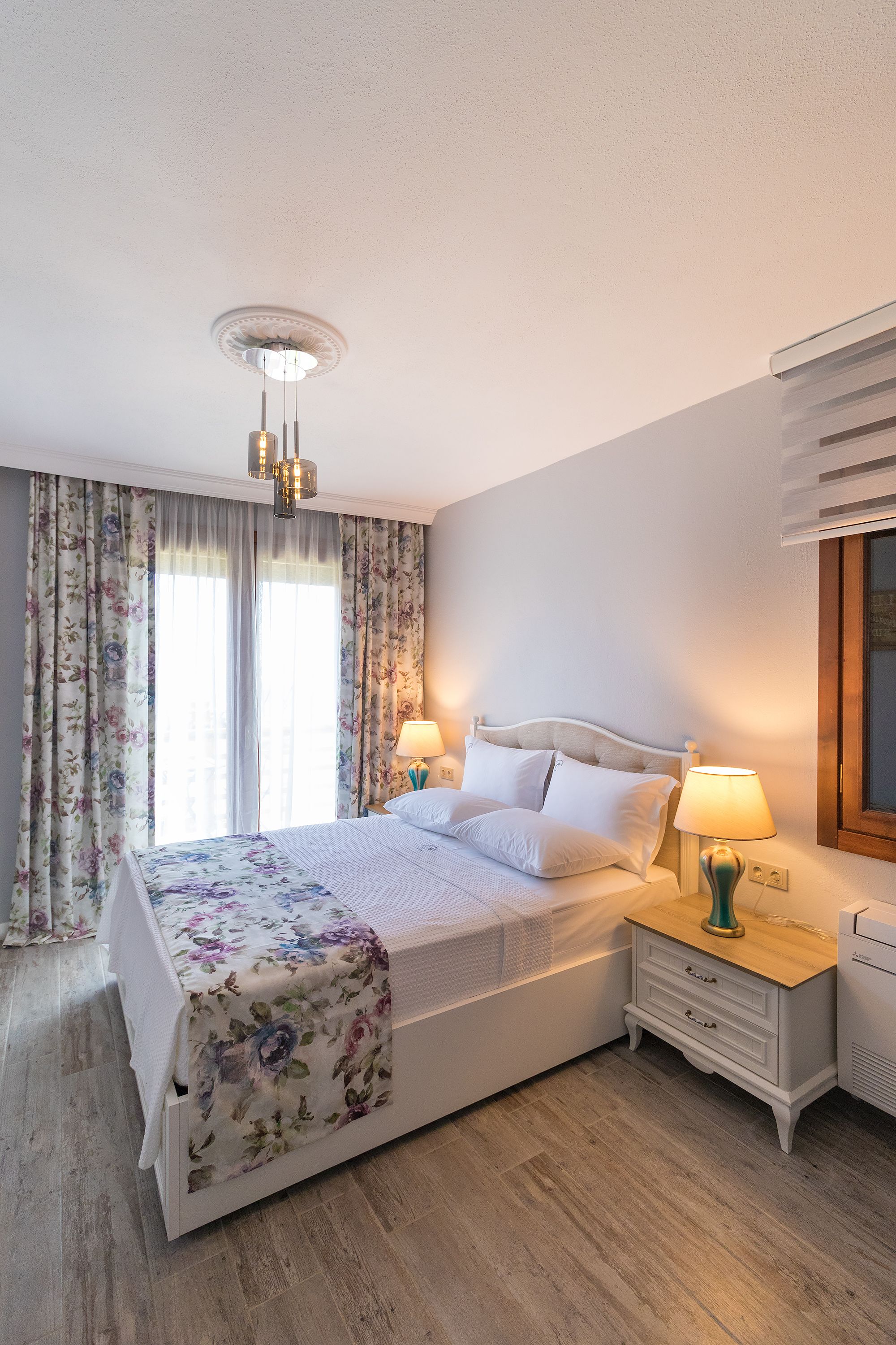 A neatly arranged bedroom with a bed, bedside lamps, a nightstand, and a window with curtains.