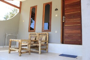 A room with a wooden door, two mirrors, a wicker chair, and a metal chair. - Join Homestay (Kuta)