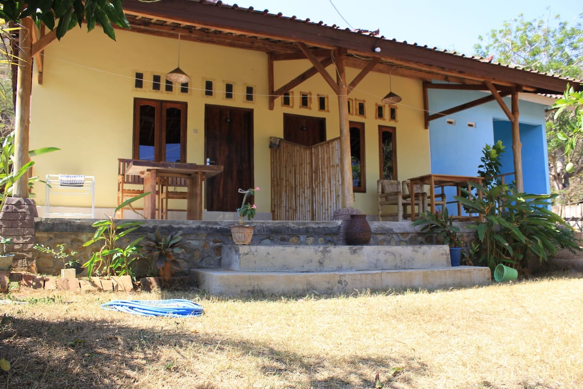 A two-story building with a porch, wooden furniture, and potted plants.