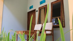 A room with two wooden chairs, a small table, and a window with curtains. - Join Homestay (Kuta)