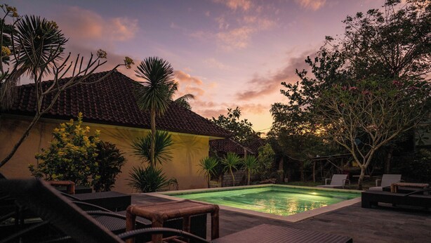 A swimming pool with lounge chairs and a tiled roof structure. - Join Homestay (Kuta)