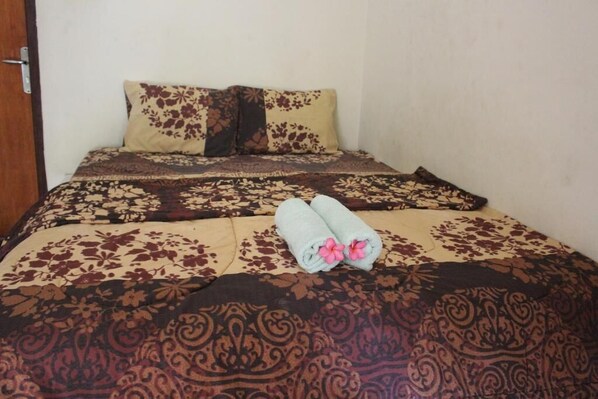 A neatly made bed with floral-patterned bedding and two towels with pink flowers.