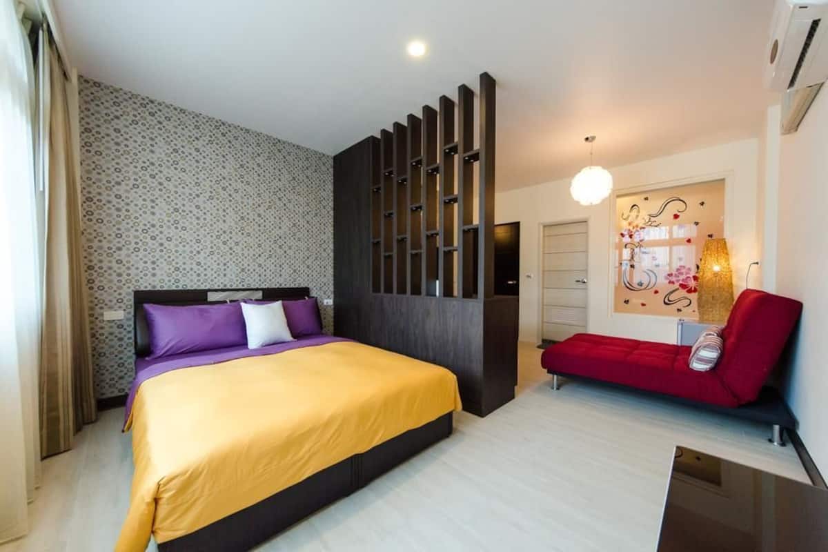 A hotel room with a bed, a red sofa, a decorative wall, and a ceiling light.