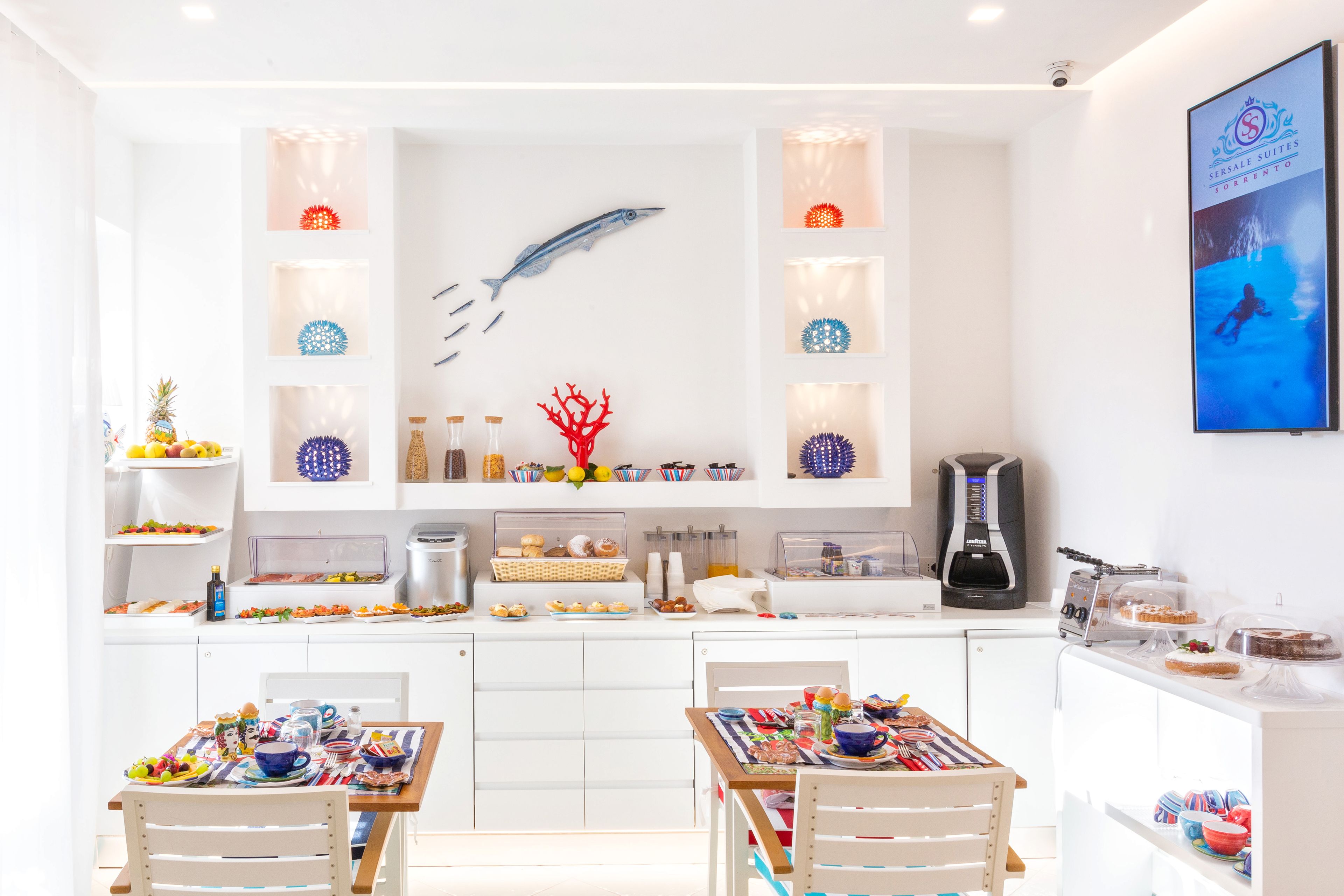 A modern kitchen with white cabinets, a coffee machine, and a variety of food items displayed on shelves and counters.