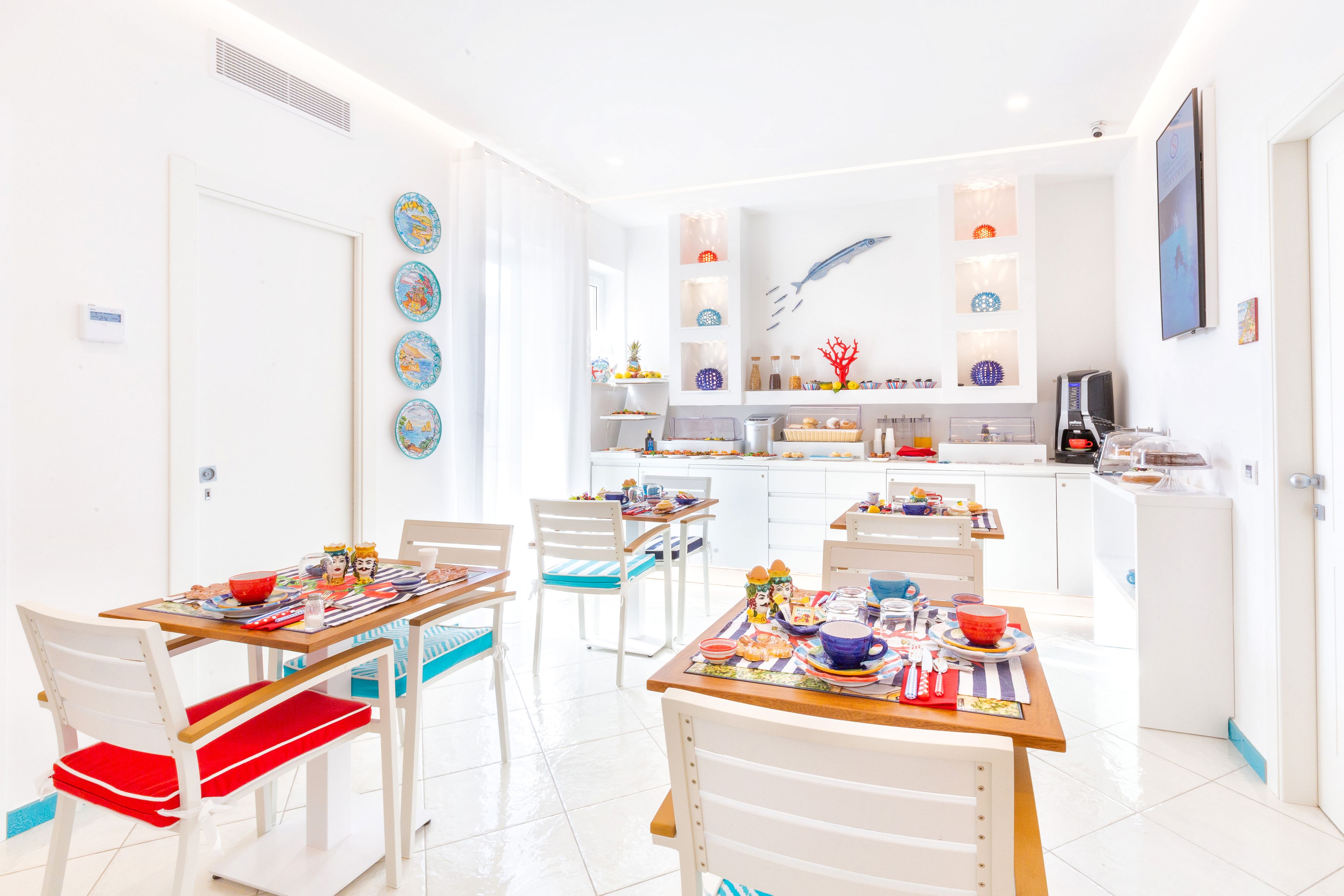A bright, modern kitchen with white cabinets, a central island, and various kitchen appliances. There are two dining areas with white chairs and a table set for a meal.