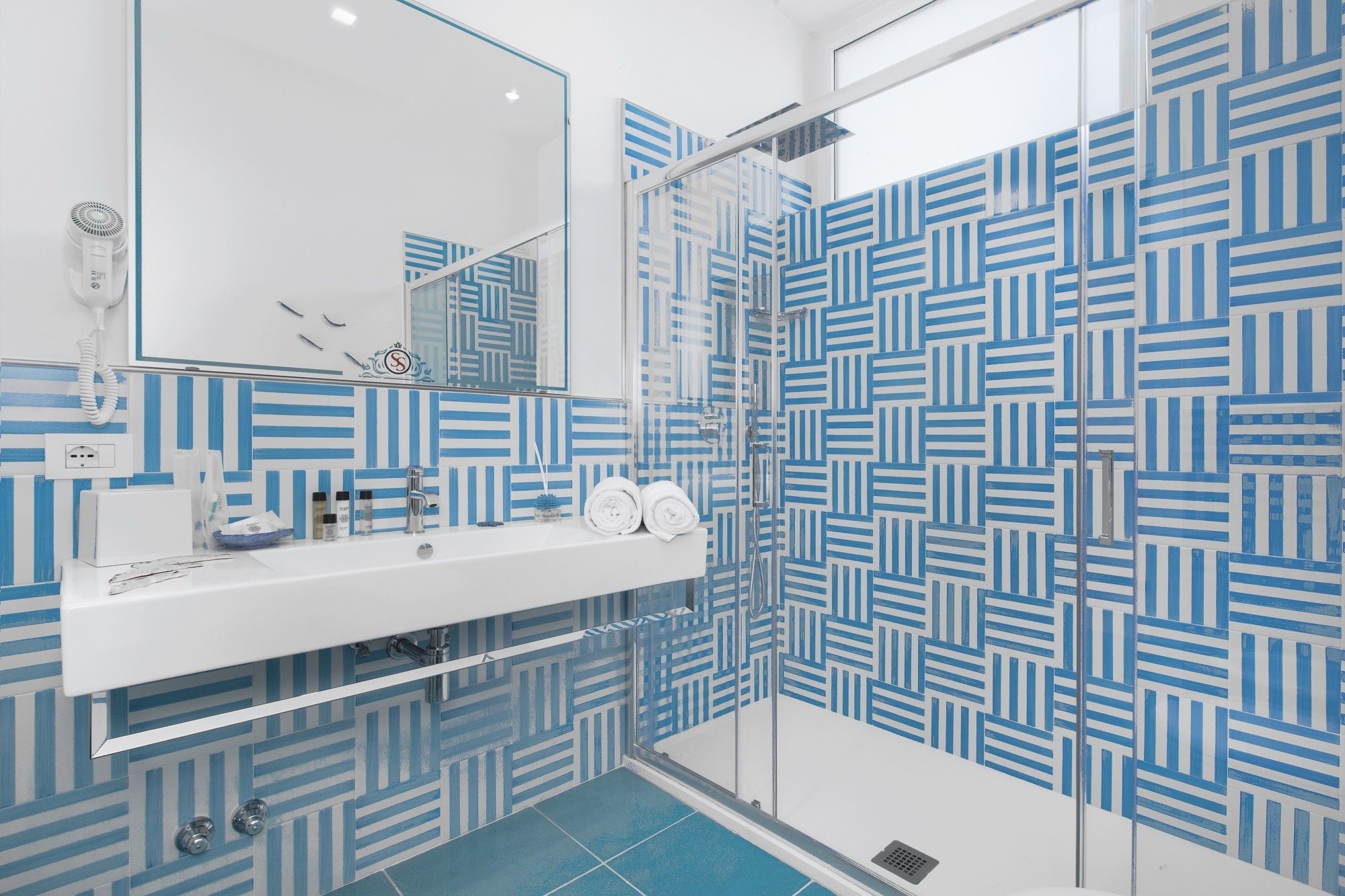 A modern bathroom with a white sink, a glass shower enclosure, and blue patterned tiles.