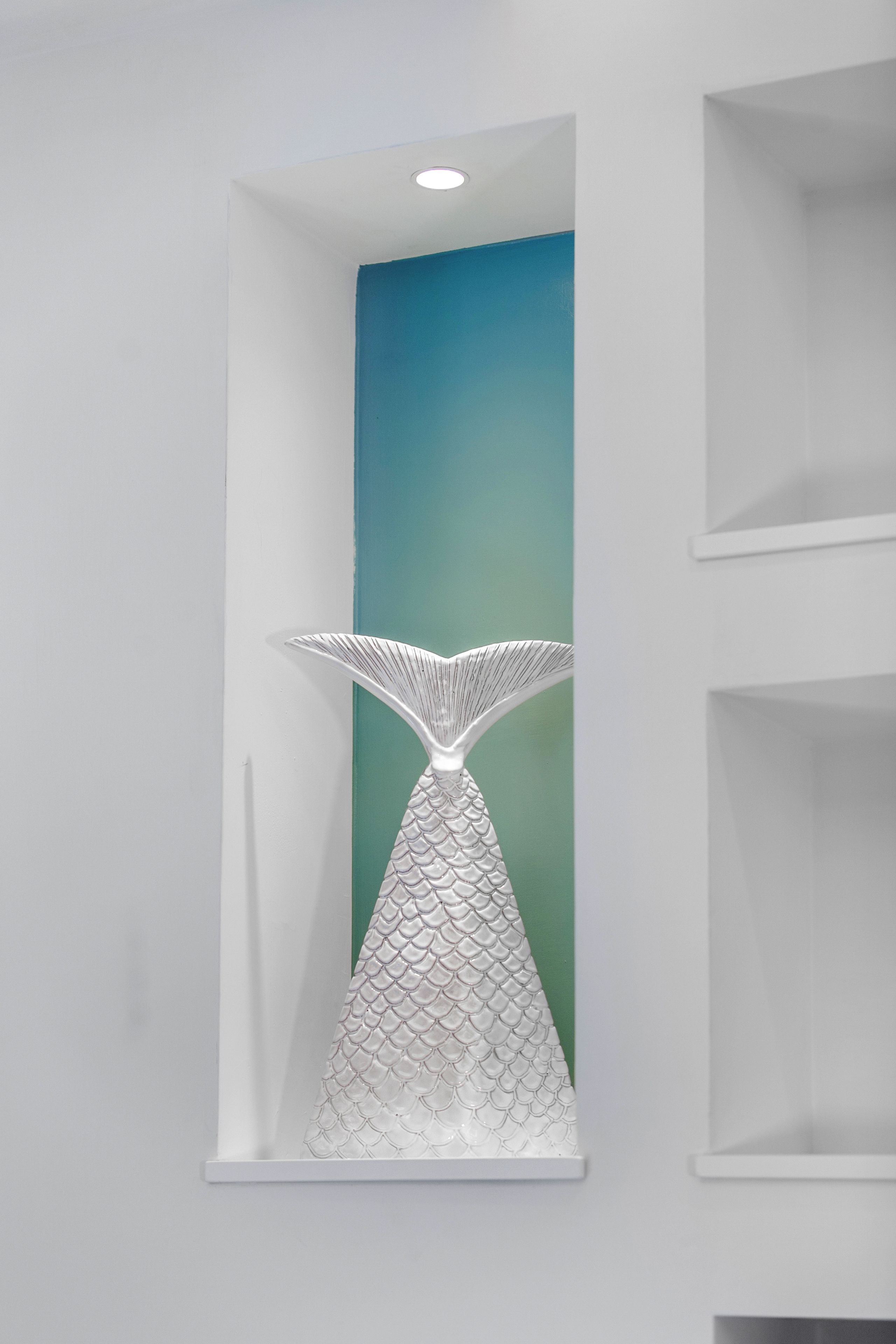 A white wall with a decorative fish tail sculpture in a white alcove.