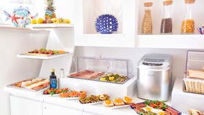 Montaje tipo bufé con diversos alimentos, una cafetera y objetos decorativos en estantes.
