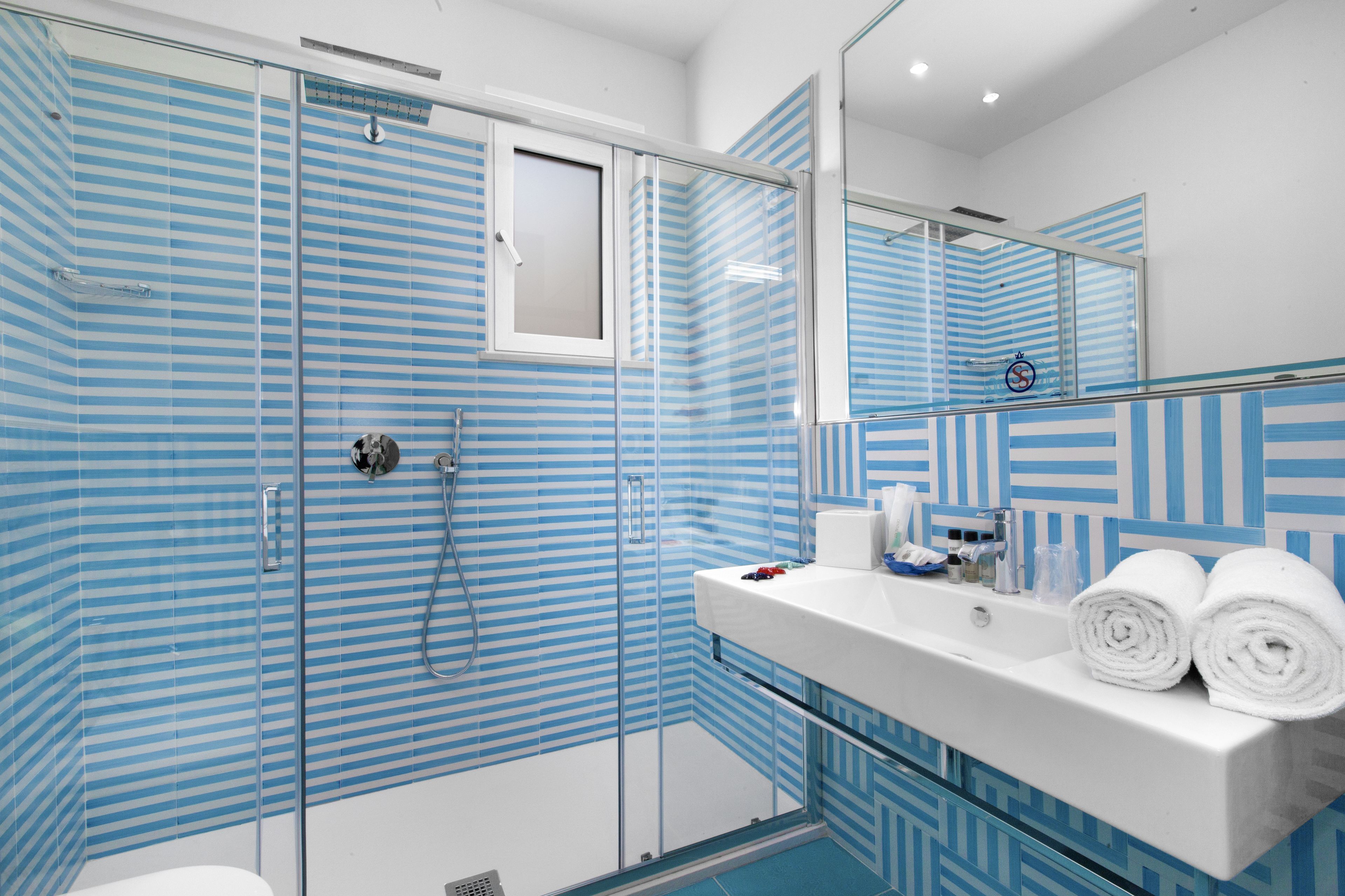 Un baño moderno con cabina de ducha de vidrio, un lavamanos blanco con artículos de aseo personal y un espejo que refleja la habitación.