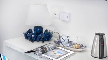 Une table blanche avec une lampe, une assiette contenant un muffin, une bouilloire et un magazine.