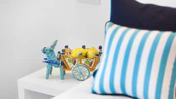 A white bedside table with a decorative ceramic horse and carriage, a striped pillow, and a white wall with a power outlet.