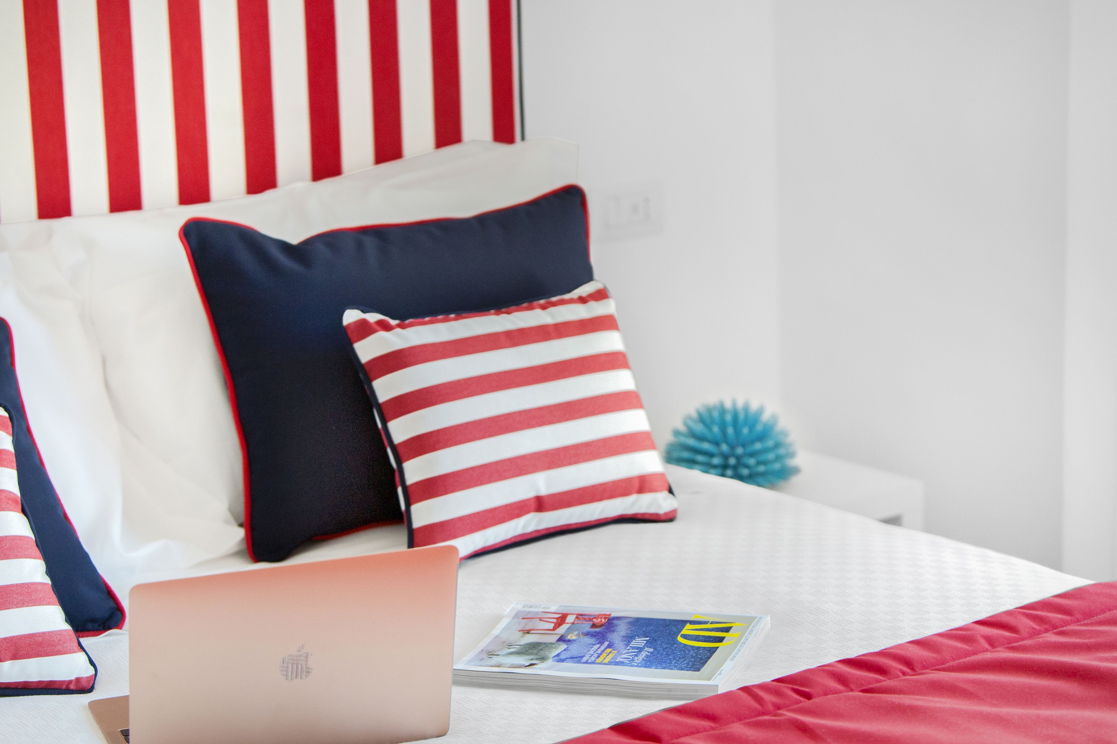 Un letto rifatto con cura, un laptop, una rivista e cuscini a righe.
