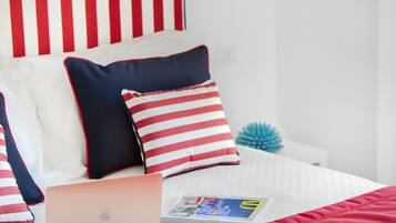 A neatly made bed with a laptop, a magazine, and striped pillows.