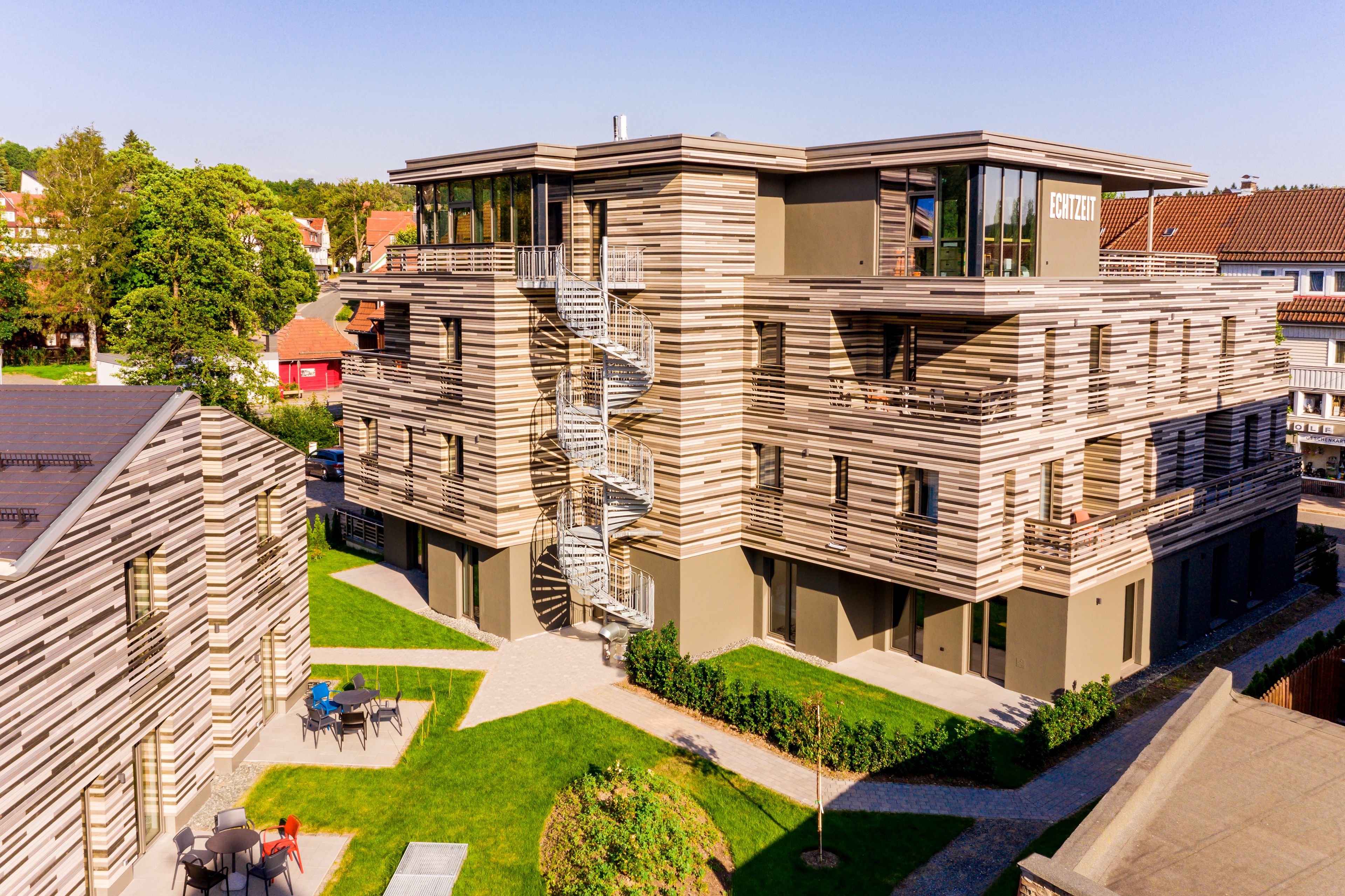 Ein modernes, mehrstöckiges Gebäude mit markantem architektonischen Design, das eine auffällige Wendeltreppe und eine Dachterrasse zeigt.
