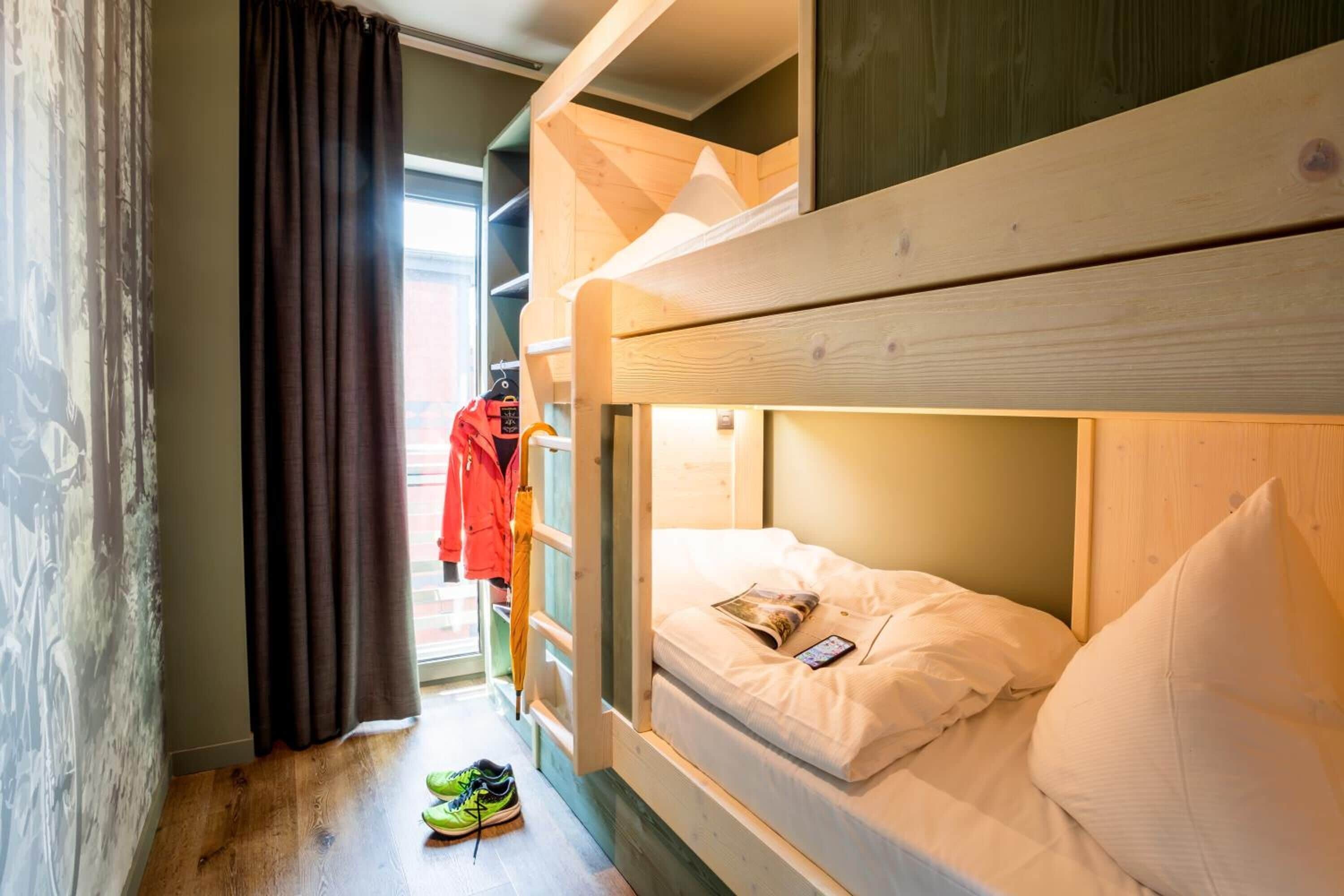 A bunk bed room with a wooden headboard, a pair of green sneakers on the floor, and a red jacket hanging on a rack.