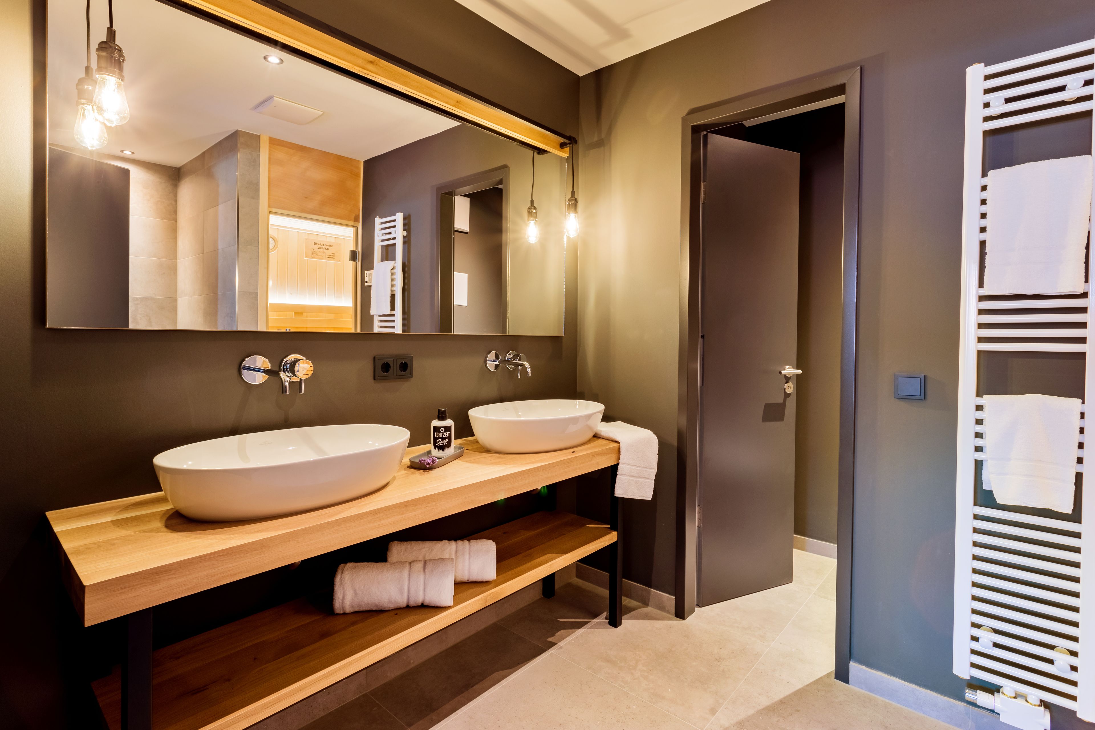 A modern bathroom with two large sinks, a wooden vanity, a large mirror, and a towel rack.