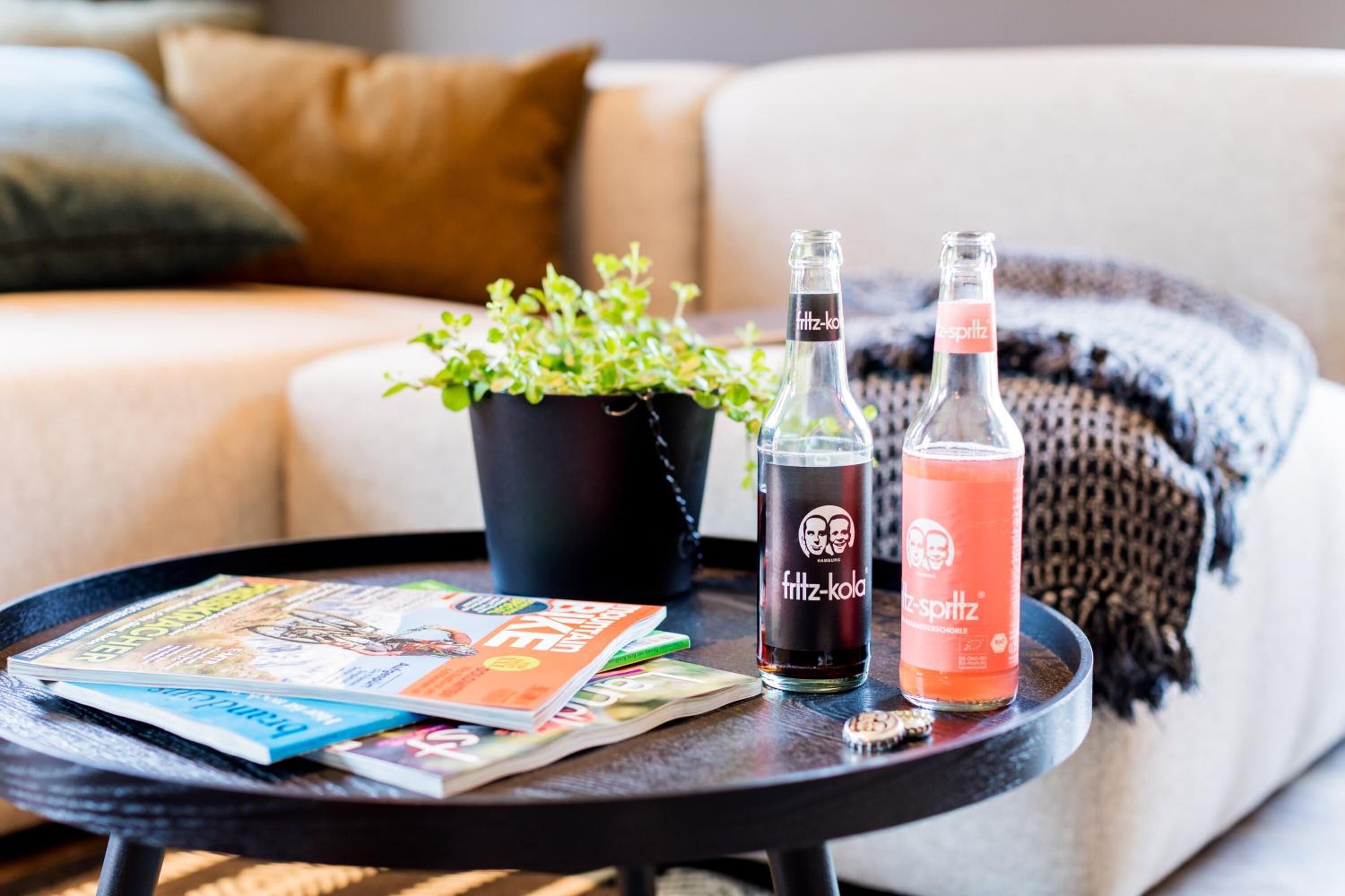 A round table with magazines, two bottles of drink, and a potted plant.
