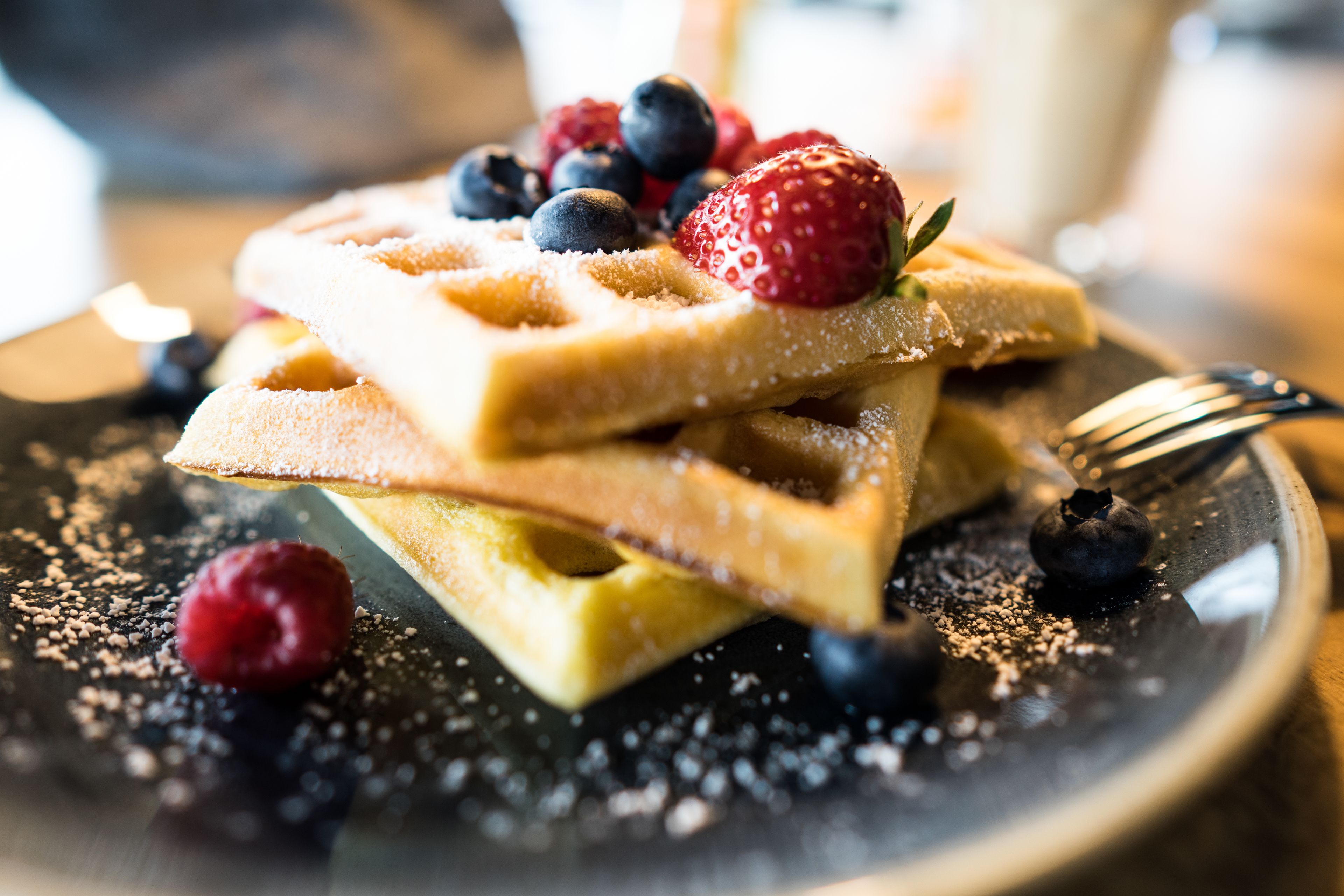 A stack of waffles with berries and powdered sugar on a plate.