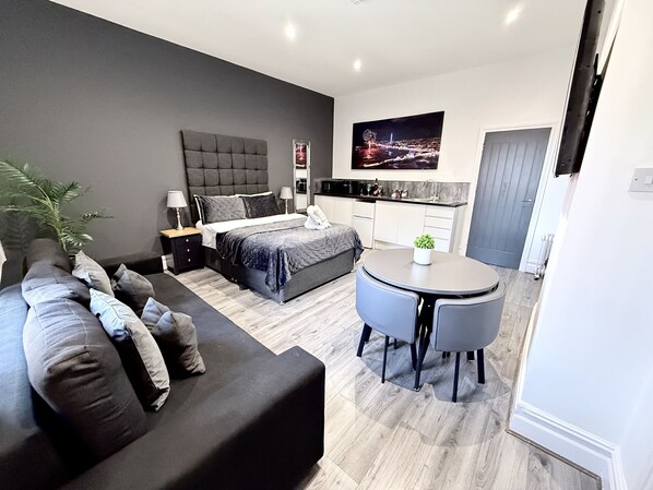 A modern bedroom with a large bed, bedside tables, a small round table with chairs, a sofa, and a view of a cityscape.