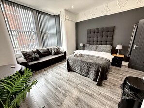 A modern bedroom with a bed, a sofa, a nightstand, a lamp, and a potted plant.