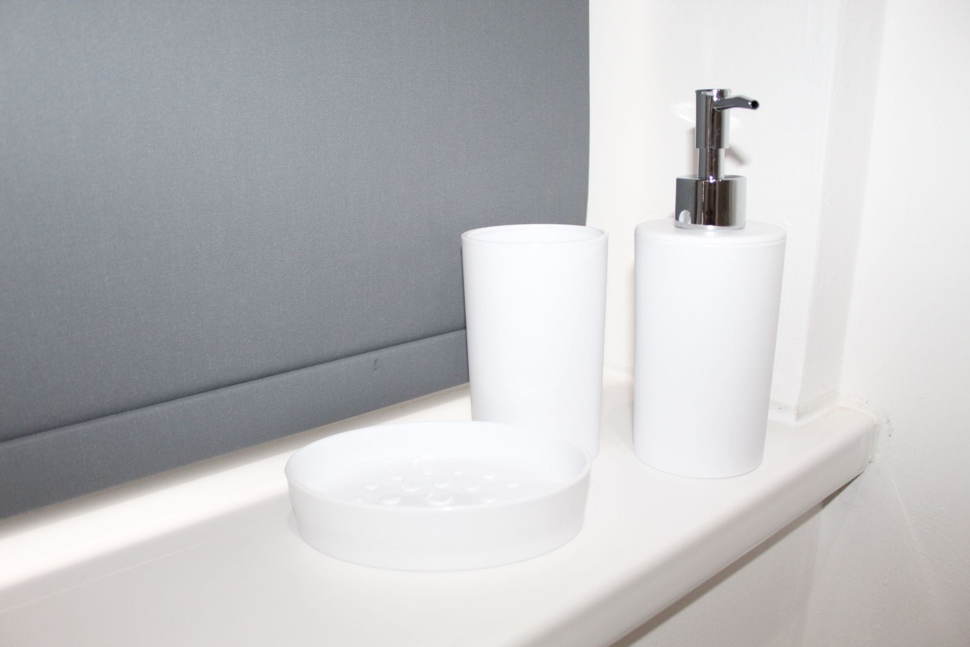 A bathroom vanity with a grey wall, a white sink, and two white dispensers.