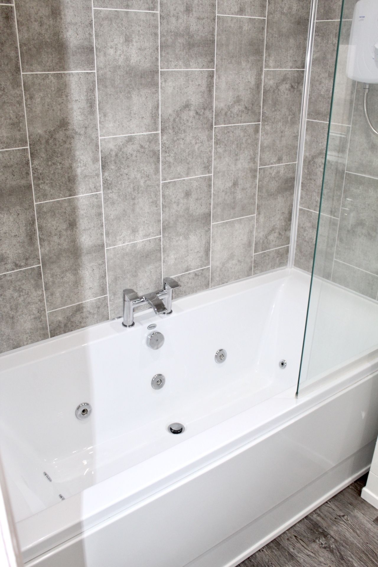 A modern bathroom with a freestanding bathtub, a glass shower enclosure, and grey tiled walls.