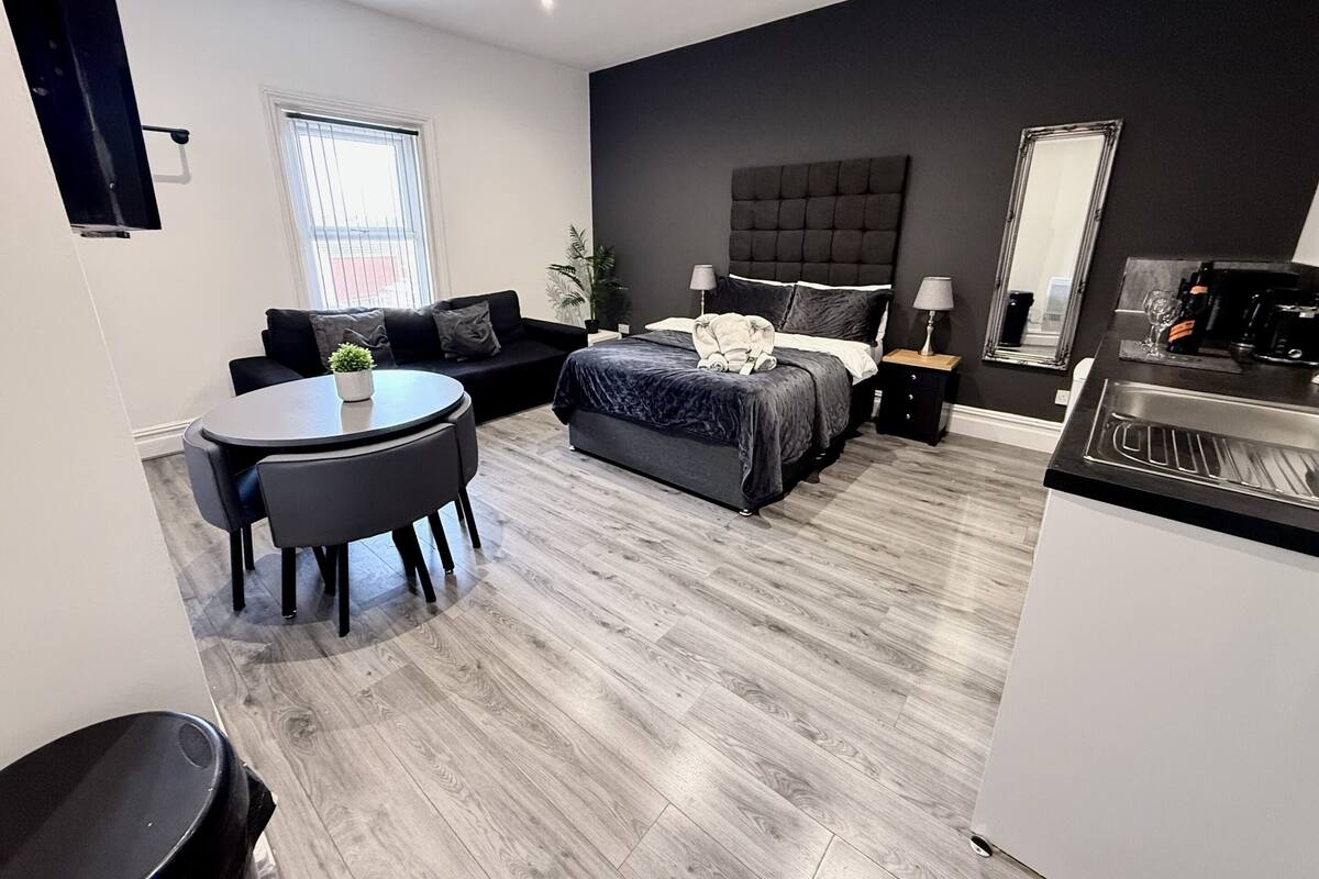 A modern bedroom with a bed, bedside tables, a round dining table, and a small kitchen area.