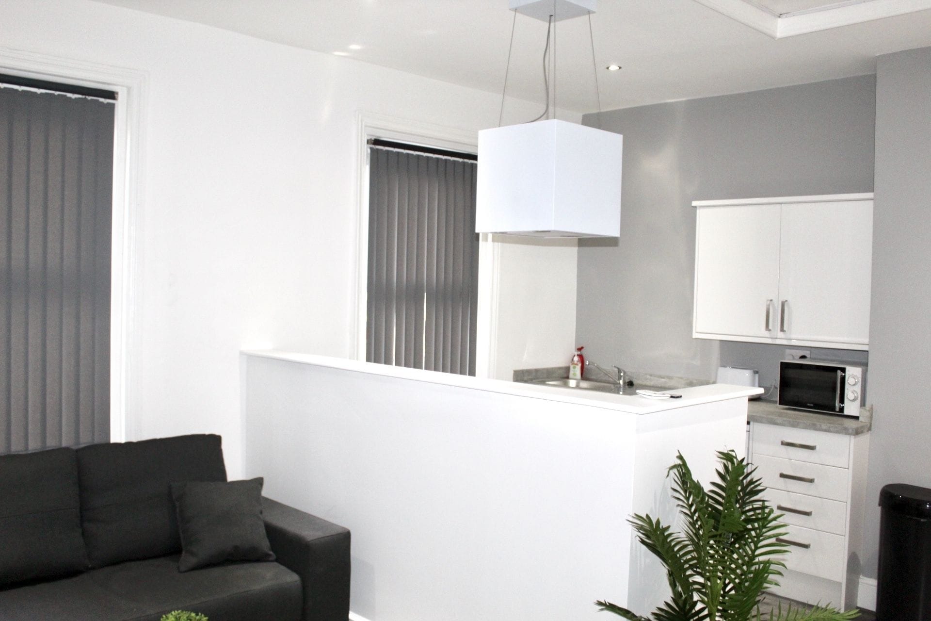 Een moderne keuken met witte kasten, een inbouwmagnetron en een hanglamp.