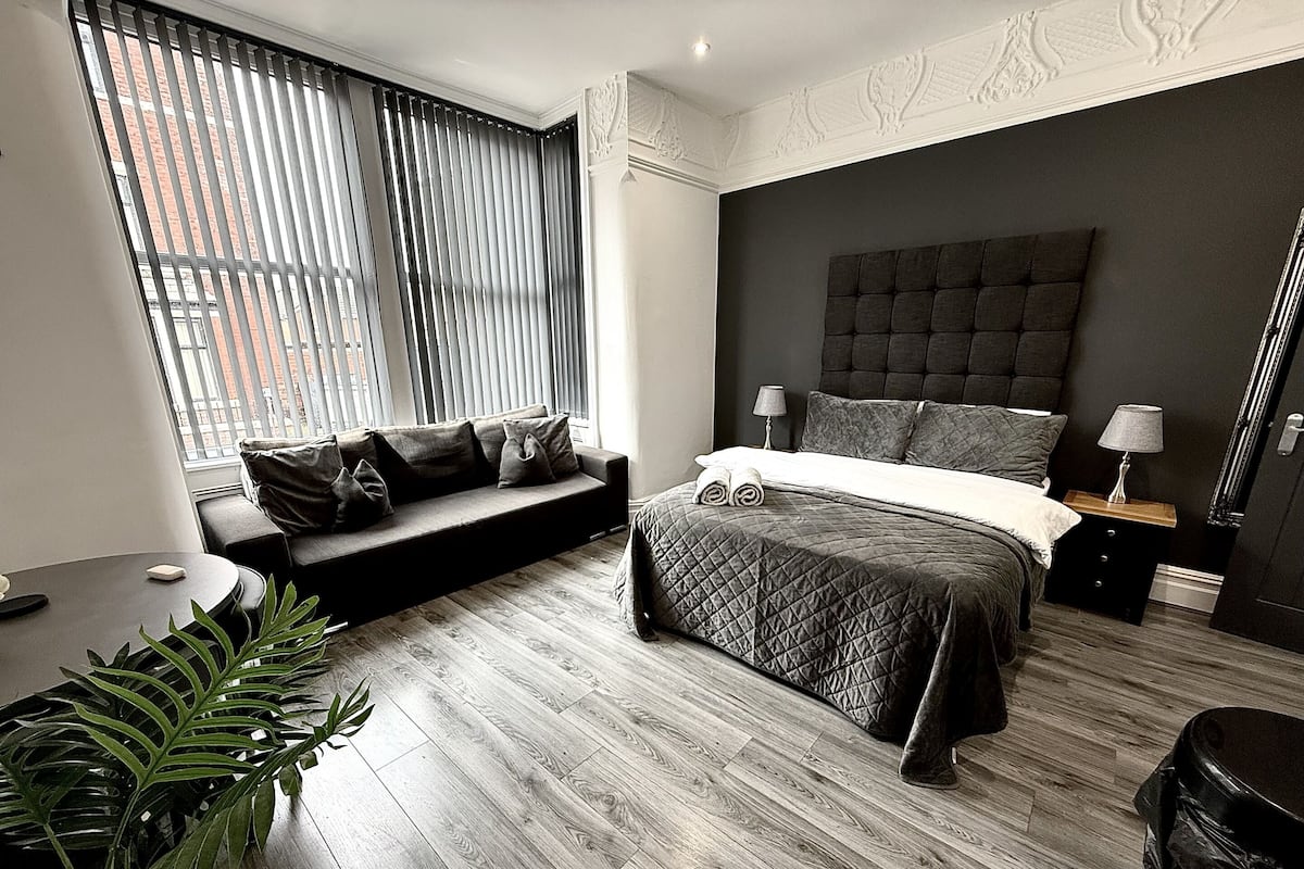 A modern bedroom with a bed, a sofa, a nightstand, a lamp, and a potted plant.