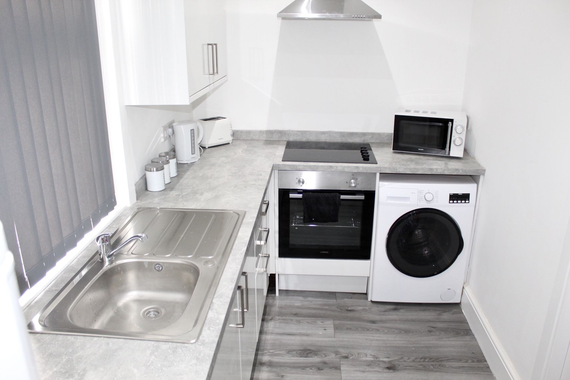 A compact kitchen with a sink, a microwave, a toaster, and a washing machine.