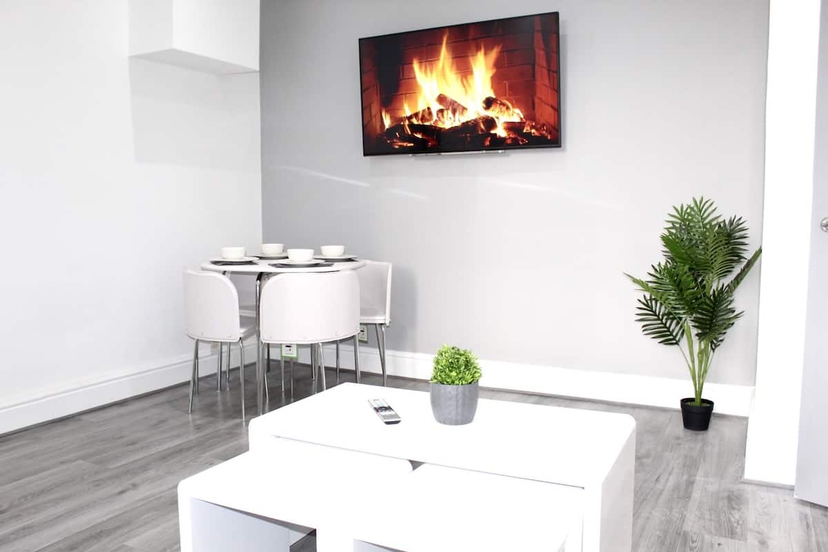A modern room with a white table, chairs, a potted plant, and a fireplace image on the wall.