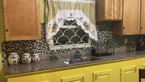 Een keuken met gele kastjes, een spoelbak en een raam met een decoratief gordijn.