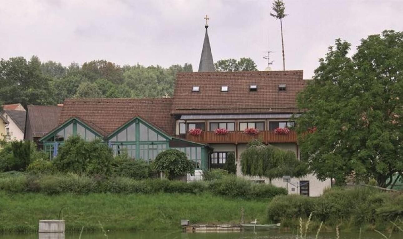 A church with a steeple, surrounded by greenery and a body of water.