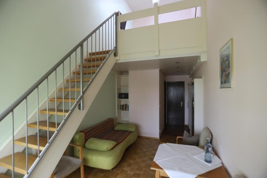 A loft-style room with a staircase, a green sofa, a small table, and a bookshelf.