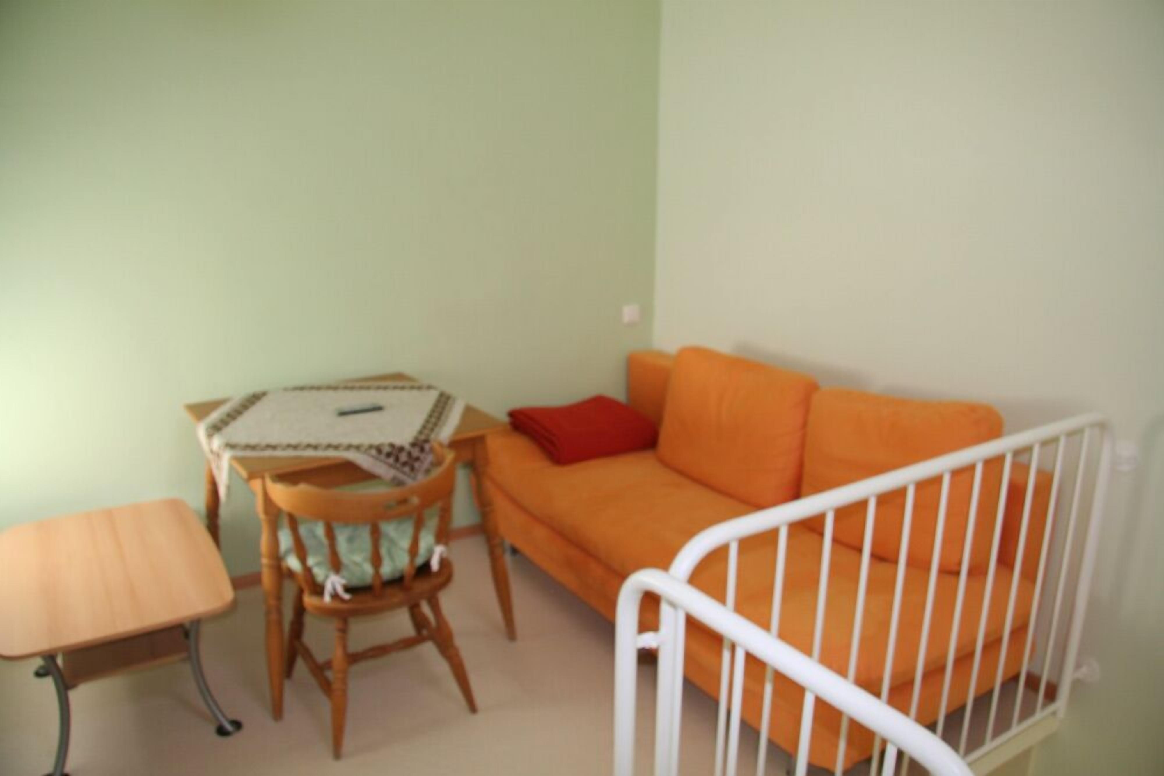 Une pièce avec une table en bois, une petite chaise, un canapé orange et un berceau blanc.