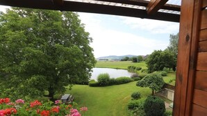 A view from a wooden balcony overlooking a well-maintained garden with a pond, trees, and a distant landscape. - Pension Krämerhof Kulz (Thanstein)