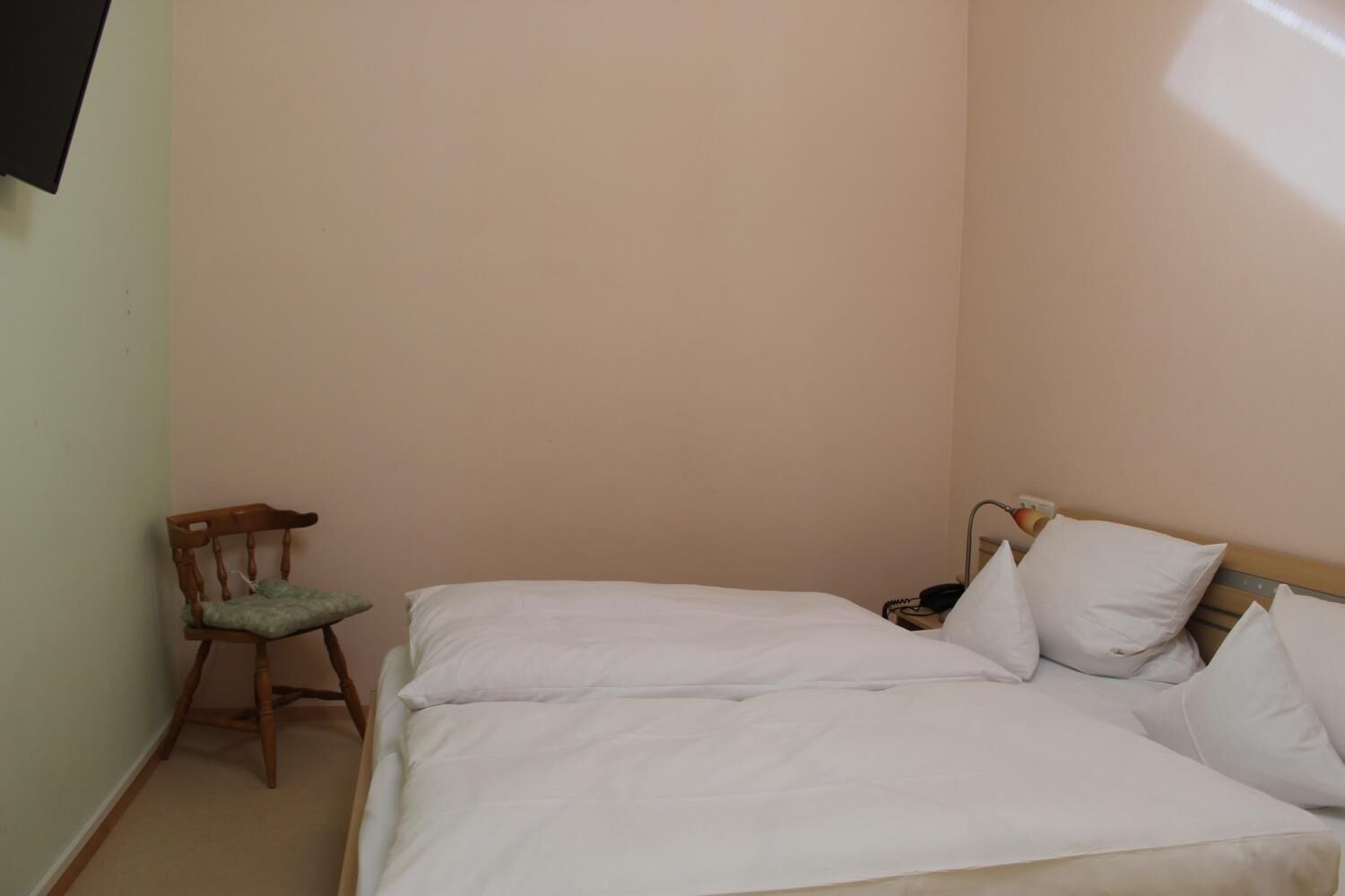 A small, neatly made bed with white bedding in a room with light-colored walls.