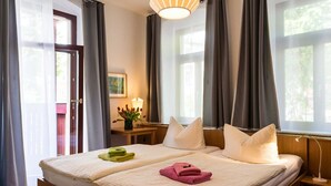 Ein Hotelzimmer mit zwei Betten, einem Nachttisch mit Lampe, einem Fenster mit Vorhängen und einer zur Außenseite führenden Tür.
