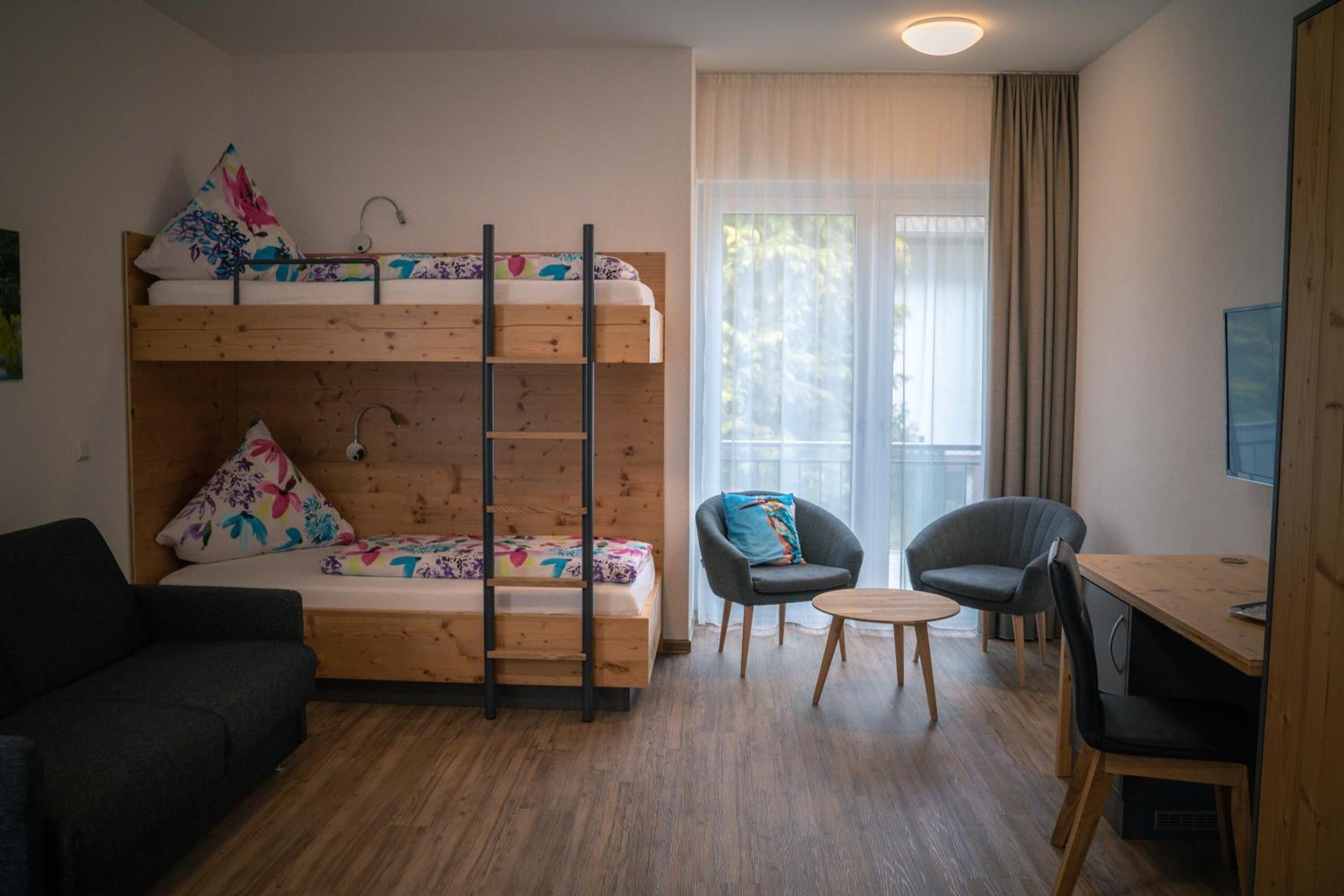A room with a bunk bed, a sofa, two chairs, a small table, and a desk with a computer.