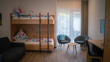 A room with a bunk bed, a sofa, two chairs, a small table, and a desk with a computer.
