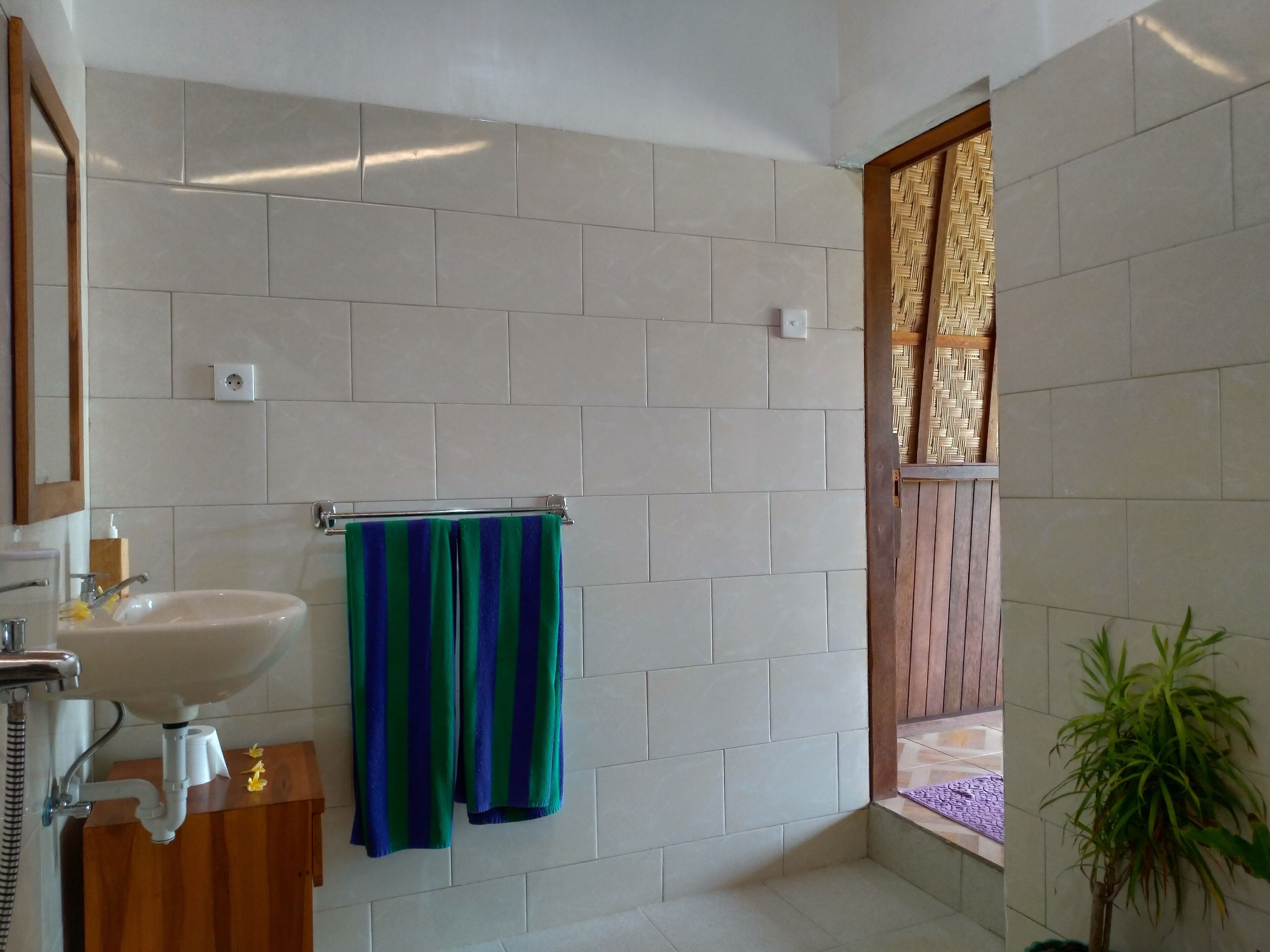 A bathroom with white tiles, a sink, a mirror, and a window with a wooden frame.
