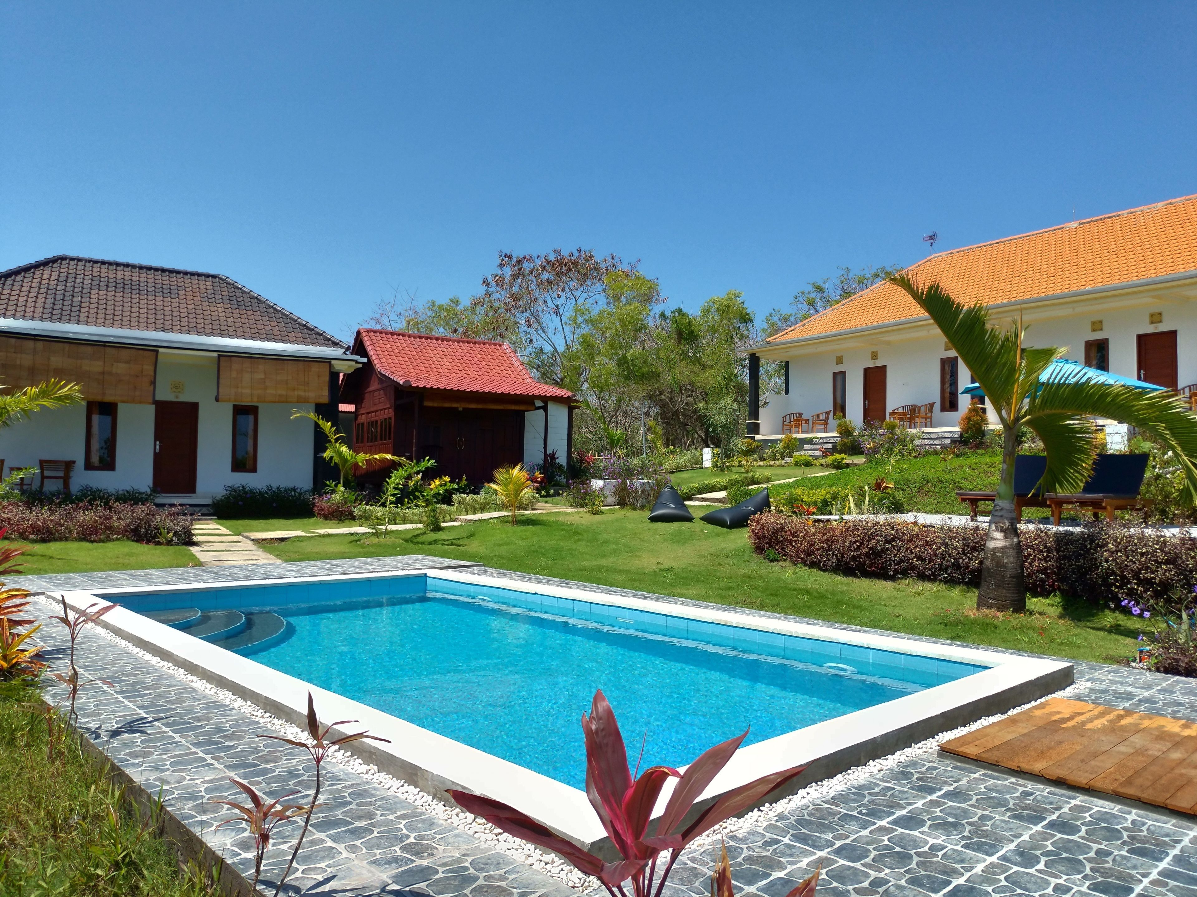 A poolside area with a swimming pool, stone-tiled deck, and surrounding greenery.