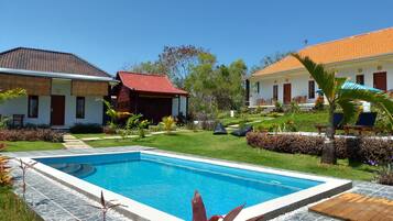 A poolside area with a swimming pool, stone-tiled deck, and surrounding greenery.