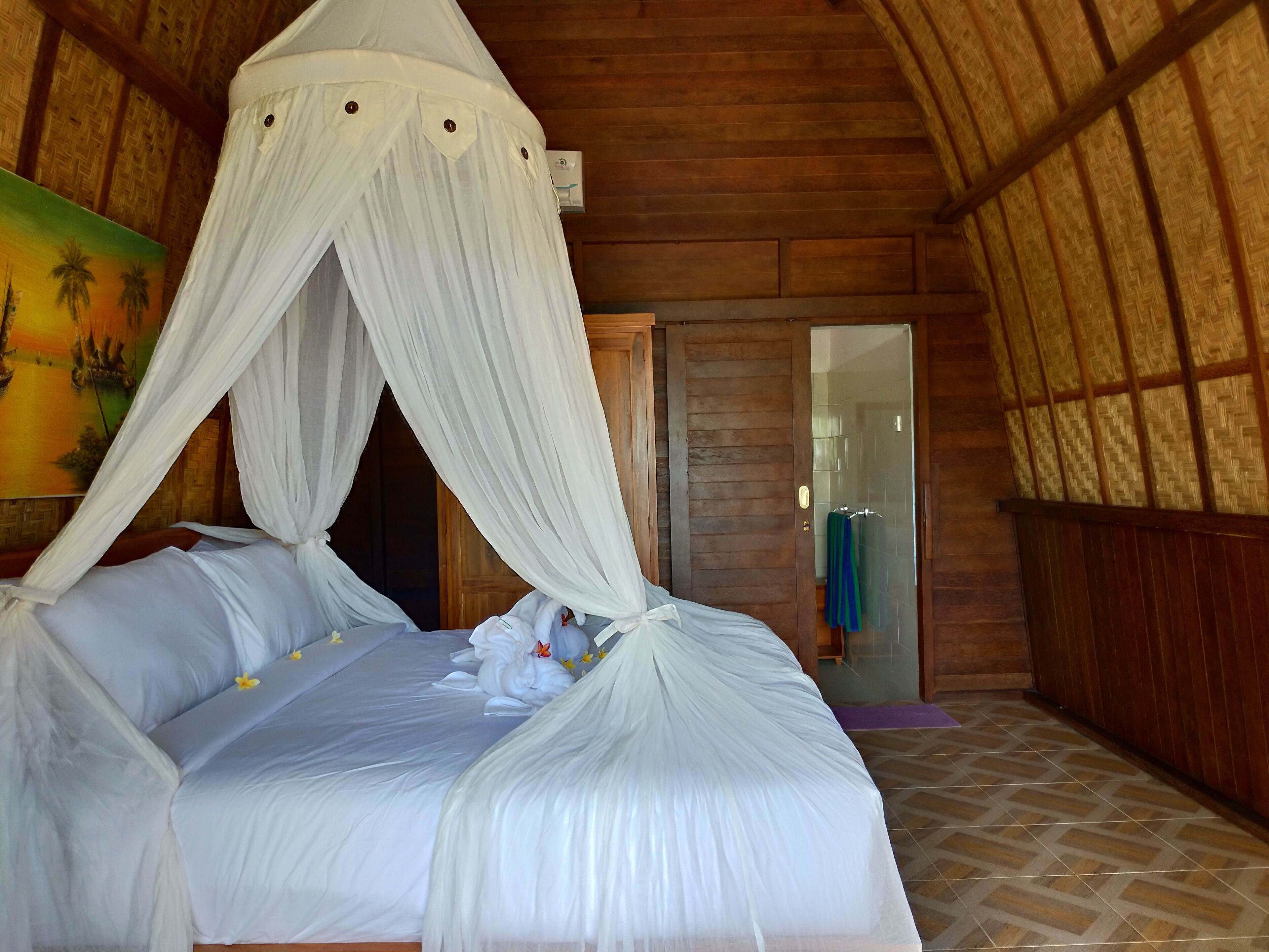 A room with a bed under a white canopy, wooden walls, and a painting on the wall.