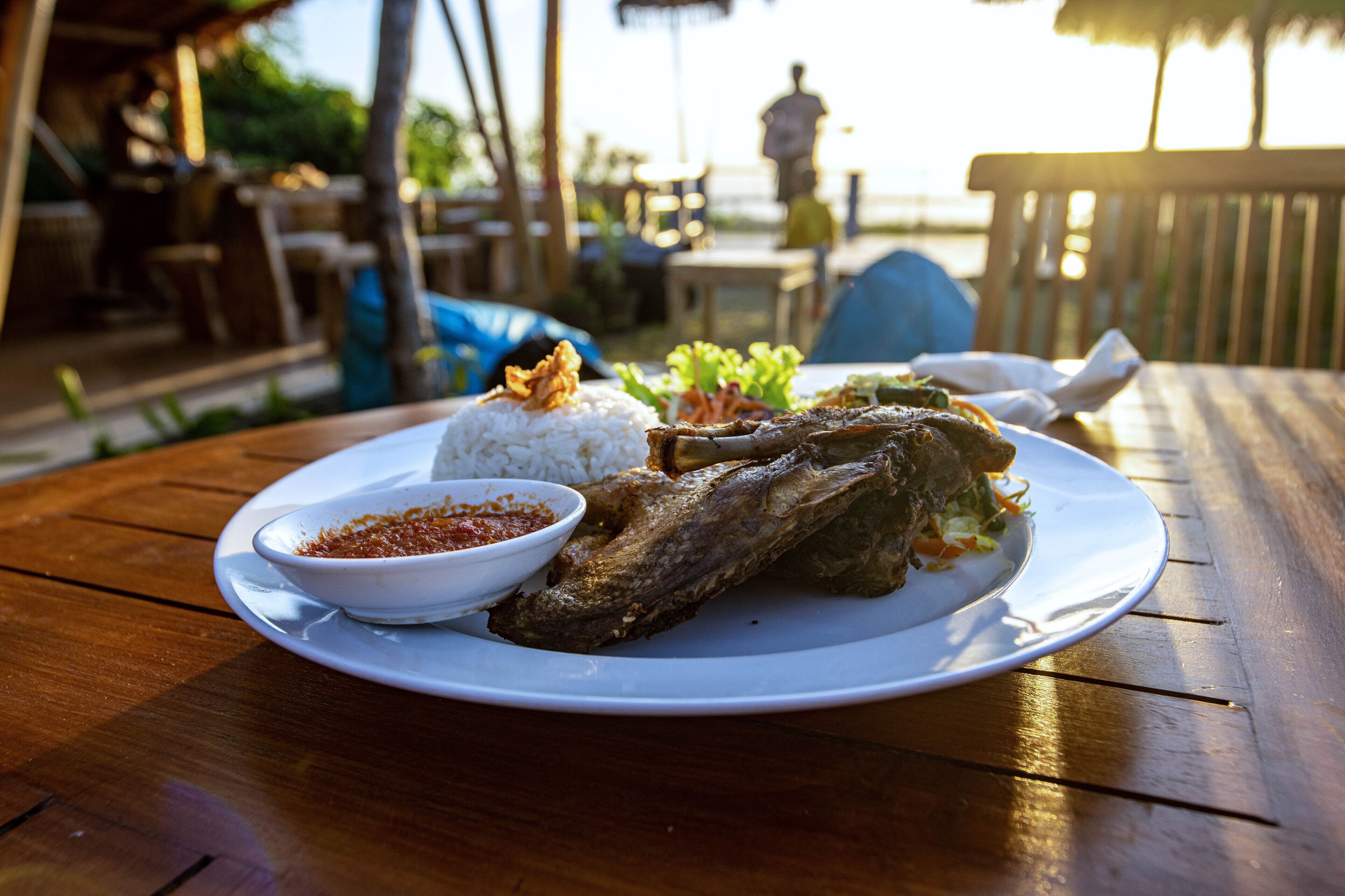 A wooden table with a plate of food including rice, a fish, and a side dish.